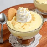Keto banana pudding served in a glass dessert cup with whipped cream, crushed cookie topping, and a keto-friendly vanilla wafer on the side.