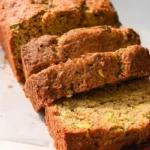 Sliced loaf from a Keto Banana Zucchini Bread Recipe, showing moist texture and golden crust on a wooden cutting board.