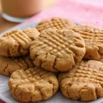 Plate of soft and chewy keto peanut butter cookies with a crisscross fork pattern, served with a glass of creamy iced coffee on a pink napkin.