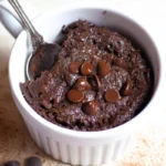 Rich and fudgy keto mug brownie recipe topped with sugar-free chocolate chips in a white ramekin with a spoon.