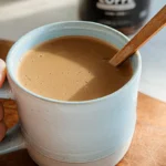 Creamy keto coffee in a light blue ceramic mug with a wooden spoon, ready to enjoy.