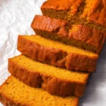 Moist keto pumpkin bread loaf sliced on parchment paper, showing fluffy golden texture.